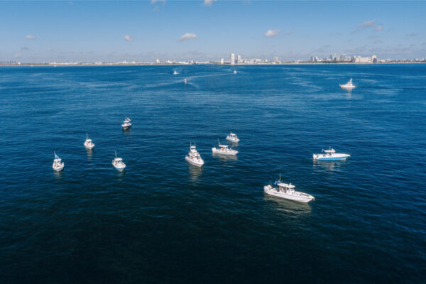 Aerial view of several Everglades boats floating on calm water with a distant city skyline under a clear blue sky