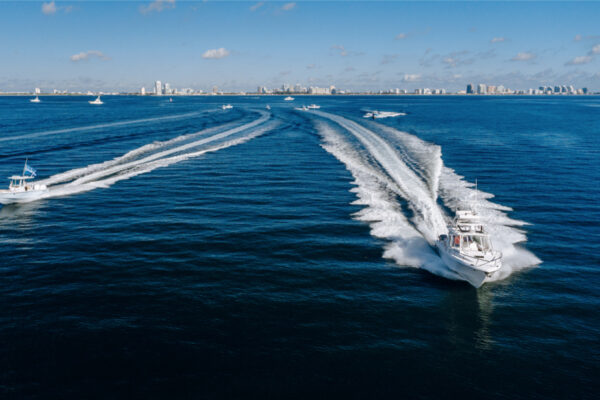 Multiple Everglades boats speeding through the water leaving wakes behind them with a distant city skyline under a clear blue sky