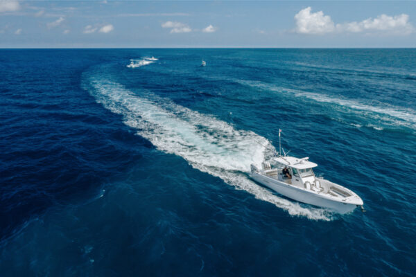 Aerial view of an Everglades boat leaving a large wake as it speeds through the open ocean with other boats visible in the distance under a partly cloudy sky