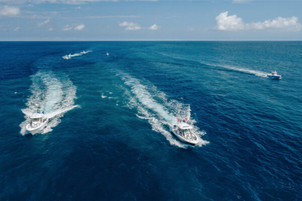 Aerial view of multiple boats speeding across the open ocean, leaving white water trails behind them
