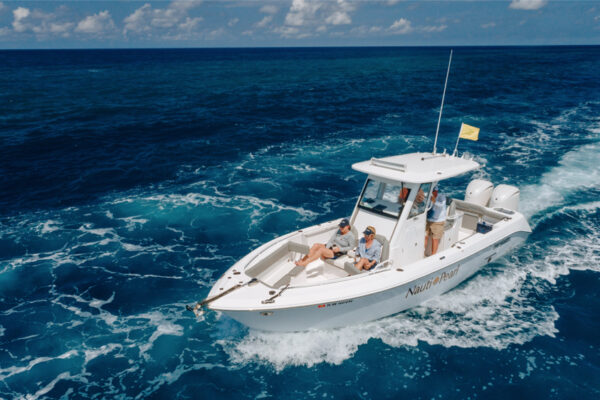 An Everglades boat cruising through deep blue water with several people on board under a partly cloudy sky