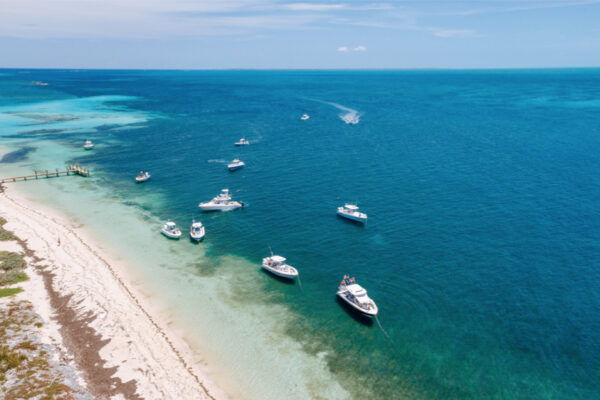Aerial view of several Everglades boats anchored near a sandy shoreline with clear blue and turquoise waters stretching into the distance under a sunny sky
