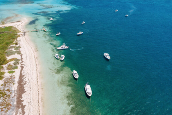 An aerial view of multiple Everglades boats anchored near a sandy beach with clear blue water surrounding them