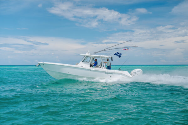 An Everglades boat speeding across turquoise water with fishing rods and flags visible and a partly cloudy sky in the background