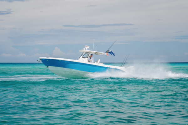 A blue and white Everglades boat speeding across turquoise water with a cloudy sky in the background
