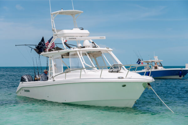 An Everglades boat anchored in shallow turquoise water with fishing rods and flags visible and another boat in the background