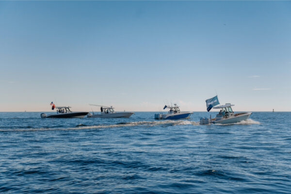 A group of Everglades boats cruising on calm water with flags flying under a clear blue sky