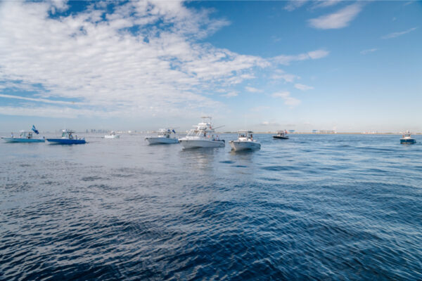 A fleet of Everglades boats on calm blue water under a sky dotted with clouds