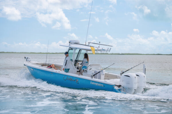 An Everglades boat cruising through the water with two people on board and fishing rods visible under a partly cloudy sky