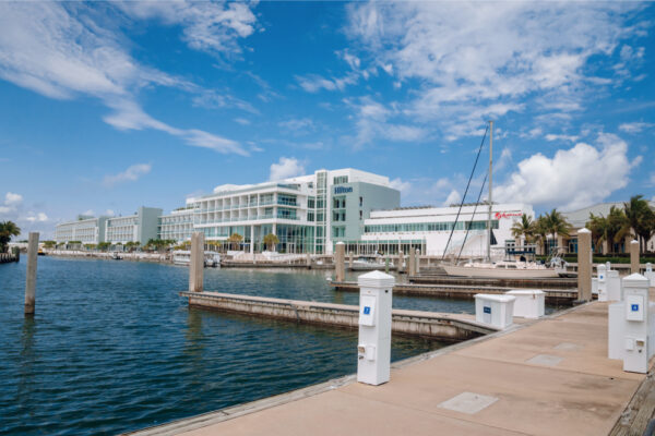 A view of a marina with empty docks and a large modern building in the background under a bright blue sky with scattered clouds