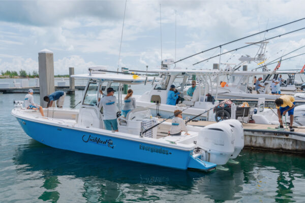 People preparing an Everglades boat at a marina dock under cloudy skies