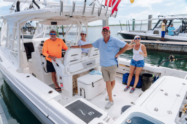 Four people standing on an Everglades boat docked at a marina with other boats visible in the background
