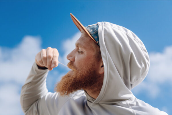 Man in a hoodie and cap against a blue sky.