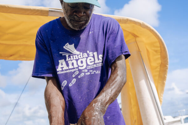 A man wearing a blue hat and a purple shirt working with his hands under a yellow canopy on a sunny day