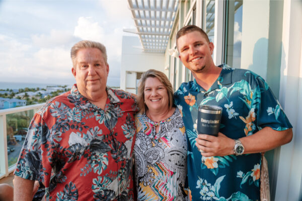 Two men and one woman in floral shirts with scenic view from a balcony