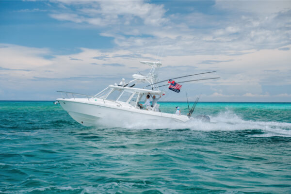Everglades fishing boat cruising on turquoise water under a cloudy sky, American flag waving