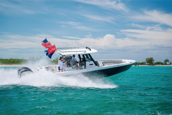 An Everglades boat speeding across turquoise water with flags flying at the back and a bright, partly cloudy sky in the background