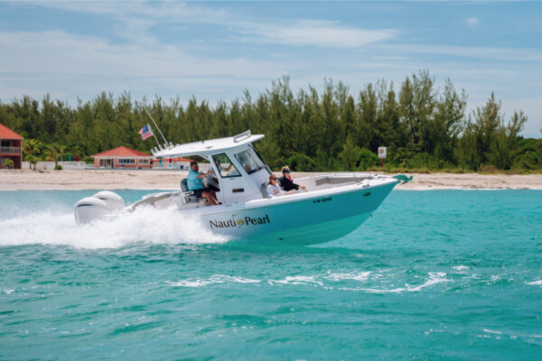 An Everglades boat speeding across turquoise water with passengers on board and a shoreline with trees and buildings in the background