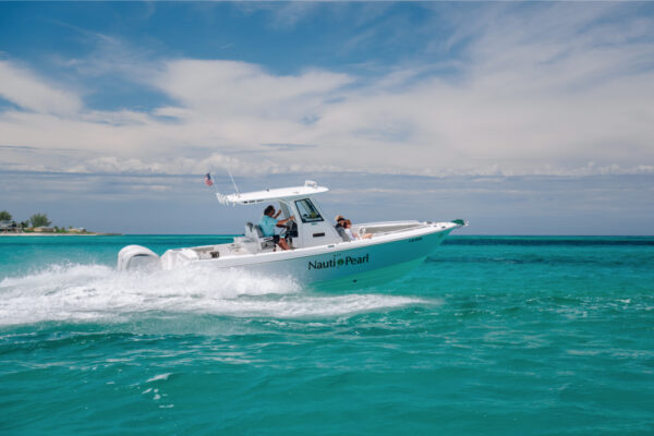 An Everglades boat speeding across turquoise water with passengers on board and a partly cloudy sky in the background