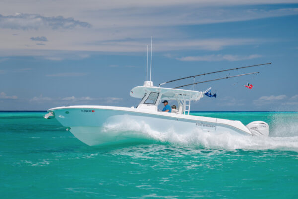 An Everglades boat speeding across turquoise water with fishing rods and flags visible under a partly cloudy sky