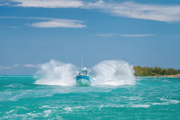 An Everglades boat creating a large splash with a shoreline and trees visible in the background under a partly cloudy sky