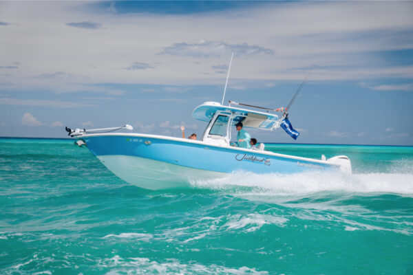 An Everglades boat speeding across turquoise water with fishing rods and flags visible and a partly cloudy sky in the background