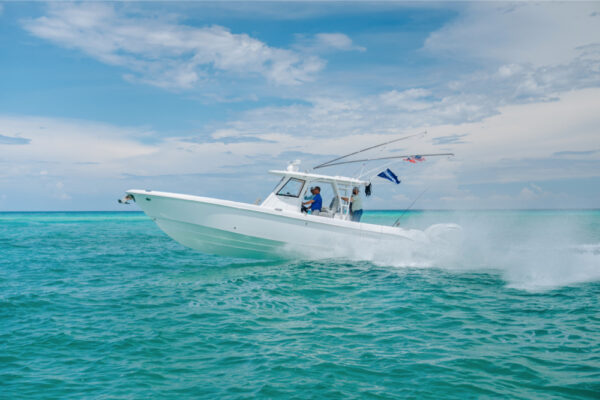 A white boat speeding across turquoise water under a partly cloudy sky, with flags flying from the rear