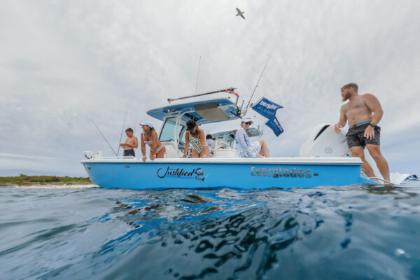 An Everglades boat with several people on board enjoying the water, fishing, and relaxing under a cloudy sky with a bird flying overhead
